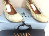 une paire de chaussures beiges ornées de nœuds, posée sur une boîte