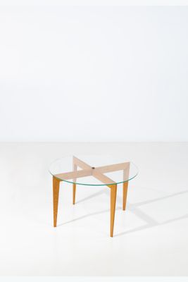une table avec un plateau en verre et des pieds en bois dans une pièce blanche