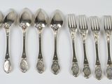 six forks and six spoons are lined up on a white surface