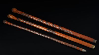 trois cannes en bois ornées de sculptures, sur fond noir