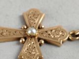 an image of a gold cross with a pearl in the center