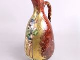 un vase rouge et doré posé sur une surface blanche