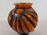 an orange vase with black stripes on it on a white surface