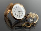 a gold pocket watch with a key on a table
