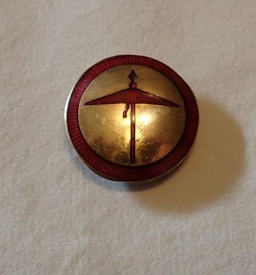 une photo d'une broche rouge et dorée sur laquelle figure un parapluie