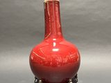a red vase sitting on a stand on a gray surface