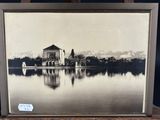 an old photo of a house on a lake with mountains in the background