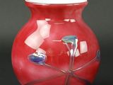 un vase rouge posé sur une table, sur fond noir