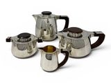 three silver teapots and two cups on a white surface