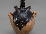un vieux vase noir et marron muni d'une anse, sur un fond gris