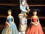 trois figurines représentant des femmes en robe et chapeau, posées sur une étagère