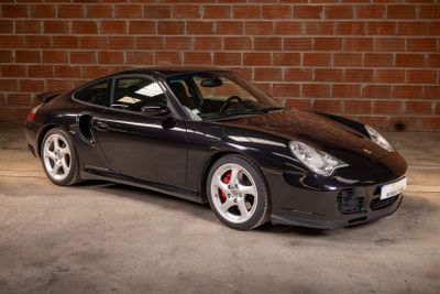 a picture of a black sports car parked in front of a brick wall