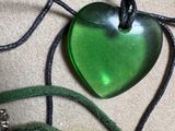 a green heart shaped glass pendant on a black cord