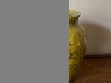 un vase jaune posé sur une table en bois près d'un mur blanc
