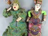 Deux petites poupées représentant des femmes en vêtements colorés sont disposées sur une surface grise.