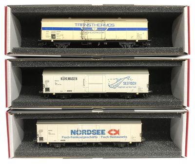 trois wagons de train miniature sont empilés dans une boîte posée sur une surface blanche