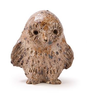 une petite figurine de chouette posée sur une surface blanche