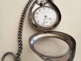 a silver pocket watch sitting on a table with a chain around it