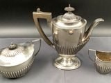 a silver tea set on a table next to a cup and saucer