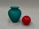 un vase bleu à côté d'une balle rouge posée sur une surface blanche