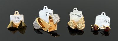 quatre types de boucles d'oreilles différents, accompagnés de leurs étiquettes de prix, posés sur une surface noire