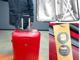 un homme debout à côté d'une valise rouge sur laquelle est accrochée une étiquette