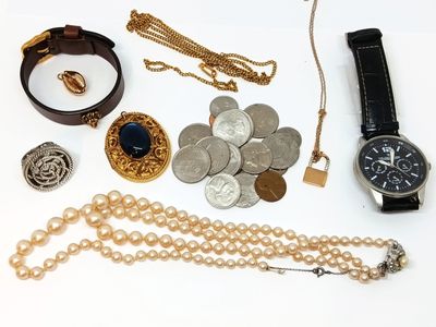 de nombreux bijoux posés sur une surface blanche, notamment une montre, des bracelets et d'autres objets