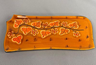 une assiette jaune ornée de fleurs et de feuilles orange, posée sur une table