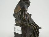 bronze statue of a woman sitting on a rock with a hat on her head