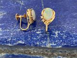 une image représentant une paire de boucles d'oreilles « oplite » posées sur une pierre bleue