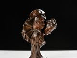 statue en bronze représentant une femme tenant un enfant dans ses bras, posée sur une surface blanche