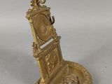 une horloge dorée posée sur un socle, sur une surface blanche