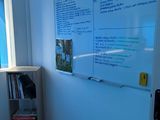 a whiteboard in the corner of a room next to a book shelf