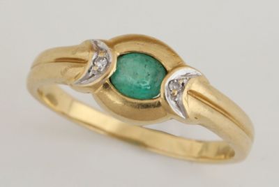 gros plan d'une bague en or avec une pierre verte et des diamants