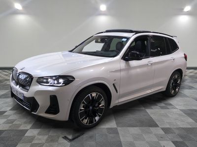 Le SUV BMW blanc est garé sur un sol carrelé à damier.