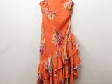 an orange floral dress hangs on a hanger against a white wall
