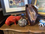un vase marron posé sur une table, avec un cochon rouge et un cochon bleu
