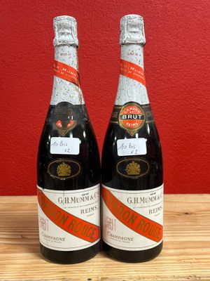 two bottles of wine sitting on top of a wooden table next to a red wall