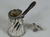 a silver cup with a wooden handle next to a pair of silver rings