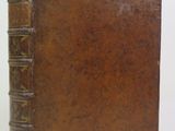 un vieux livre brun posé sur une table à côté d'un mur blanc
