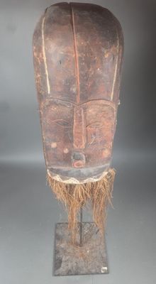 un vieux masque en bois posé sur un socle, sur une surface grise