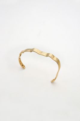 un gros plan d'un bracelet manchette en or sur fond blanc