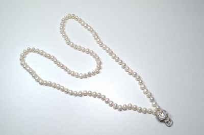 un collier de perles blanches muni d'un fermoir en argent, posé sur une table blanche