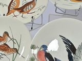 four plates with birds painted on them sitting on a table