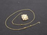 a gold necklace with a chain that has a small piece of gold on it