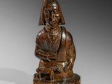 une vieille statue en bois représentant une femme assise sur un tabouret
