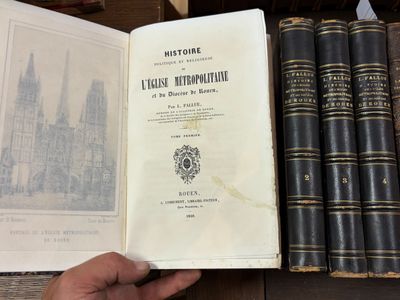 une personne tenant un livre devant une pile de livres posés sur une étagère