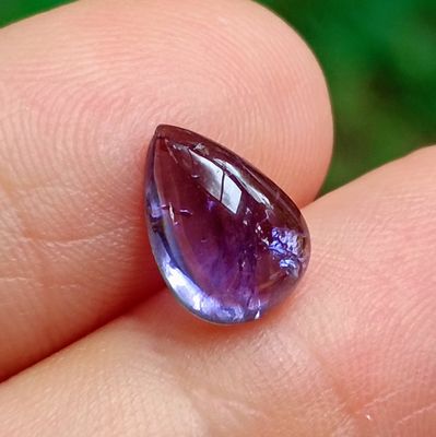 une personne tient une pierre précieuse violette dans la main, sur un fond vert