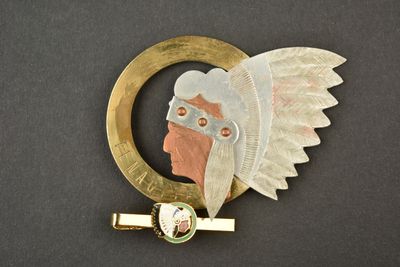 une photo d'une broche représentant un homme avec une plume sur la tête