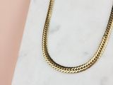 un gros plan d'un collier à chaîne en or posé sur une surface en marbre